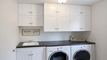 A laundry room with two front-loading washing machines, a sink, and a sign that reads "Wash and Dry Laundry Service."