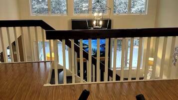 A spacious room with a wooden floor, a large window with a view of snow-covered trees, and a ceiling fan.