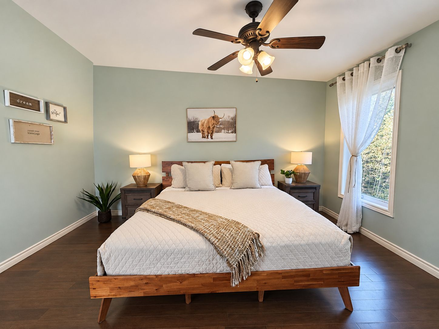 A bedroom with a bed, two bedside tables, a ceiling fan, a window with curtains, and wall art.