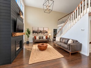 A modern living room with a fireplace, a large sofa, a coffee table, and a staircase.