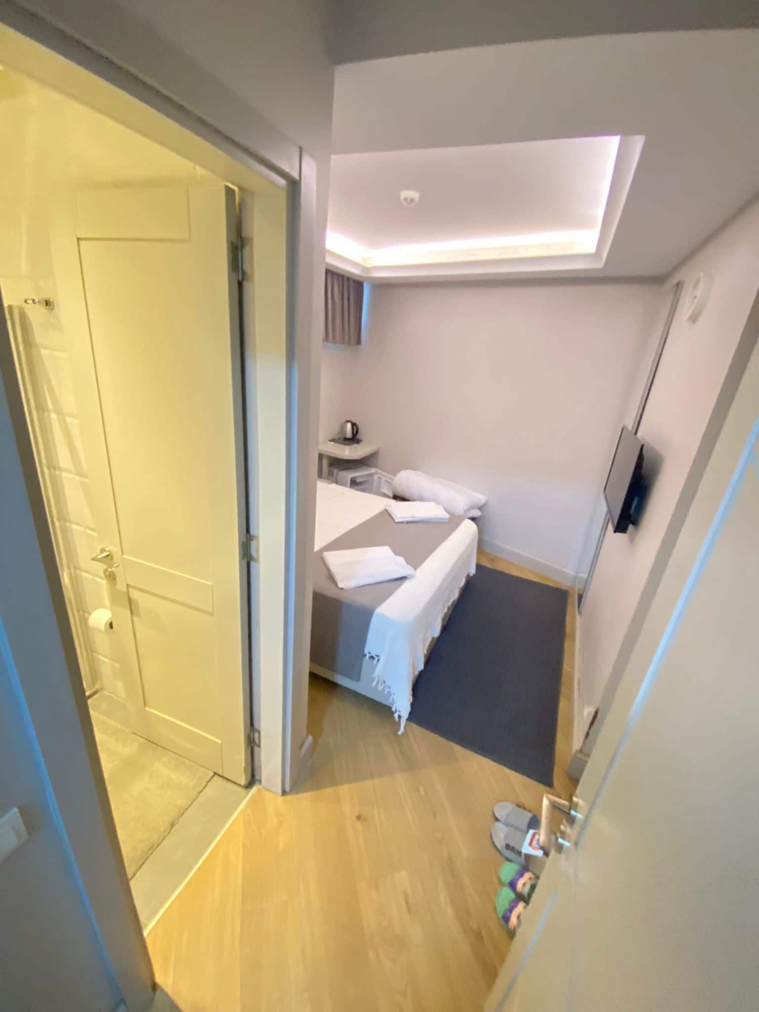 Moderni hotellihuone, jossa on sänky, pieni työpöytä, litteänäyttöinen televisio ja kattovalaisin.