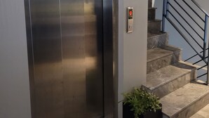 An elevator with a metallic finish, a wall-mounted intercom, and a staircase with a black railing. - Konak Bella 3 (Istanbul)