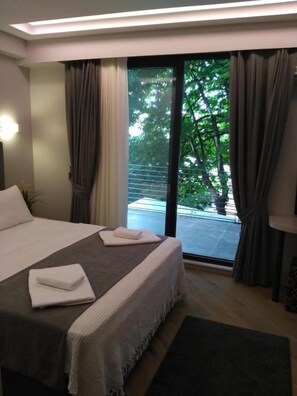 A modern hotel room with a large bed, a view of the outdoors through a sliding glass door, and a small side table with a lamp. - Konak Bella 3 (Istanbul)