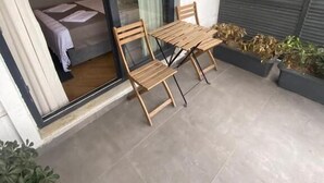 A modern outdoor seating area with a table and chairs, a glass door leading to a room, and a view of the street. - Konak Bella 3 (Istanbul)