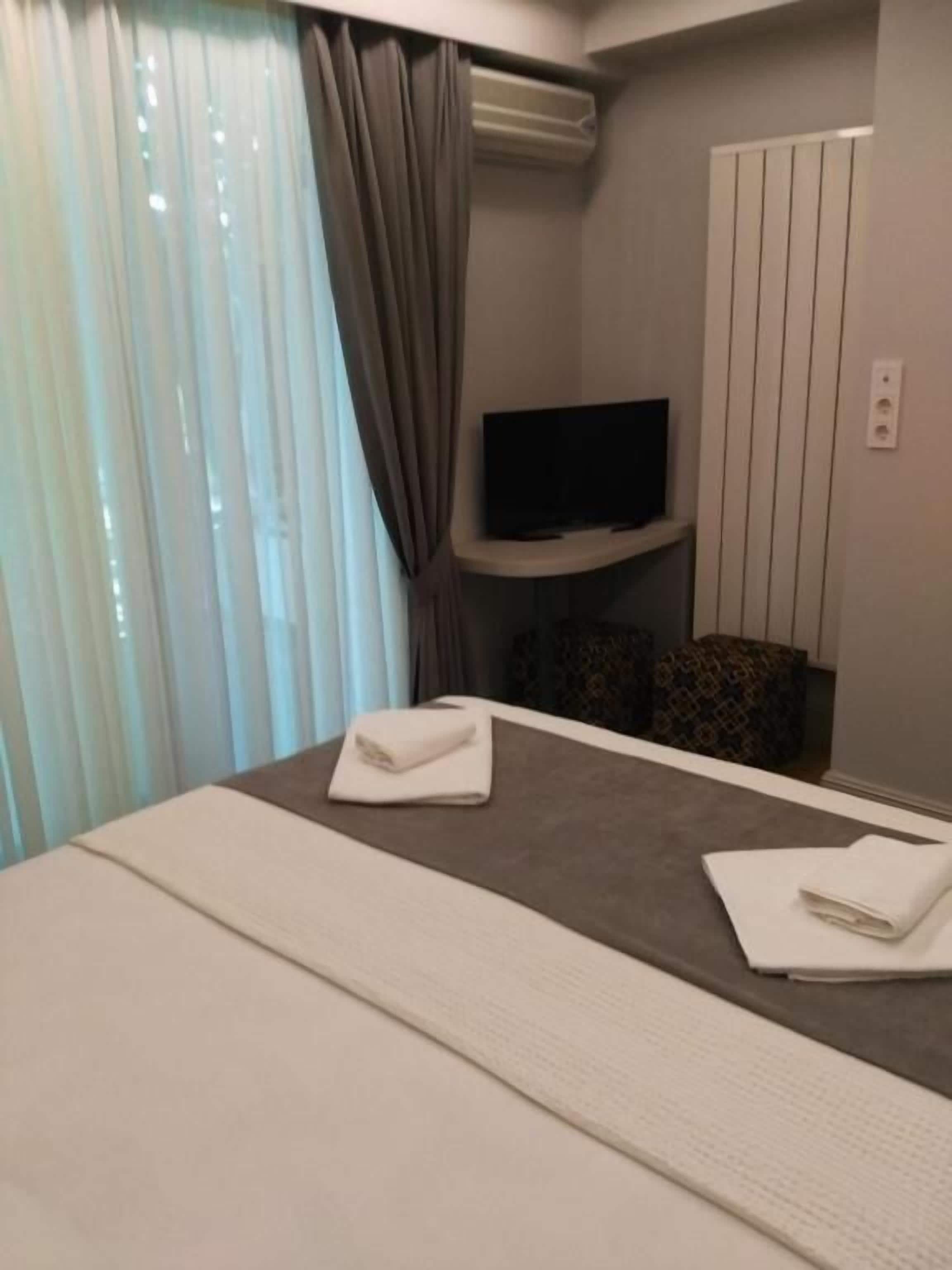 Ein Hotelzimmer mit Bett, einem an der Wand befestigten Flachbildfernseher und einem Fenster mit Vorhängen.