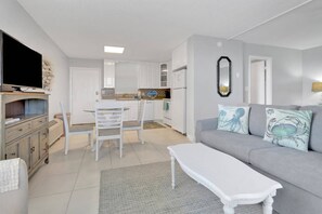 Uma sala de estar moderna com um sofá cinza, mesa de centro branca e uma TV sobre um suporte de madeira.