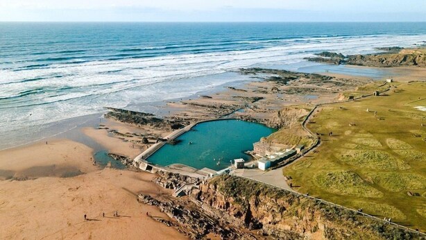 Luchtbeeld van een kustgebied met een strand, een groot waterlichaam en een klein eiland met gebouwen.