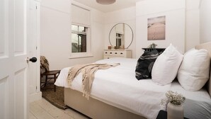Een slaapkamer met een bed, een dressoir, een spiegel, een raam en een deur.
