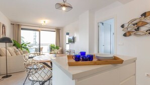 A modern kitchen with a central island, a dining area with a round table and chairs, and a balcony with a view.