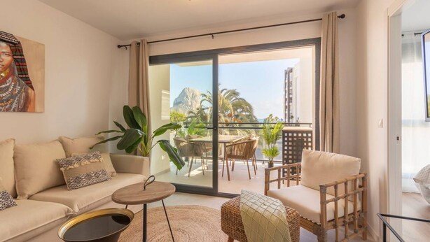 A modern living room with a sofa, armchairs, a coffee table, and a balcony with outdoor furniture.