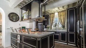 Une cuisine dotée d’un îlot central, de meubles de rangement noirs, d’une grande horloge et d’une fenêtre avec des rideaux.