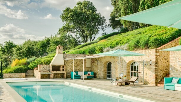 Un espace aménagé au bord de la piscine, avec un mur en pierre, des sièges d’extérieur et un barbecue.