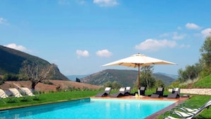 Ein Poolbereich mit Liegestühlen und Sonnenschirm, eingebettet in eine reizvolle Landschaft mit Hügeln.