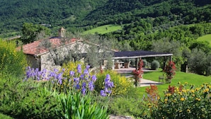 Ein Steinhaus mit rotem Ziegeldach, umgeben von üppigem Grün und farbenprächtigen Blumen.
