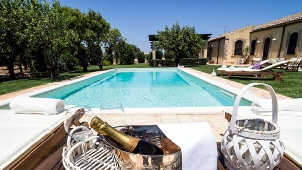Une piscine avec des chaises longues et une bouteille de champagne.