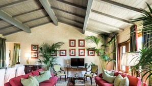 Un salon spacieux avec un plafond haut, un téléviseur et plusieurs fauteuils.