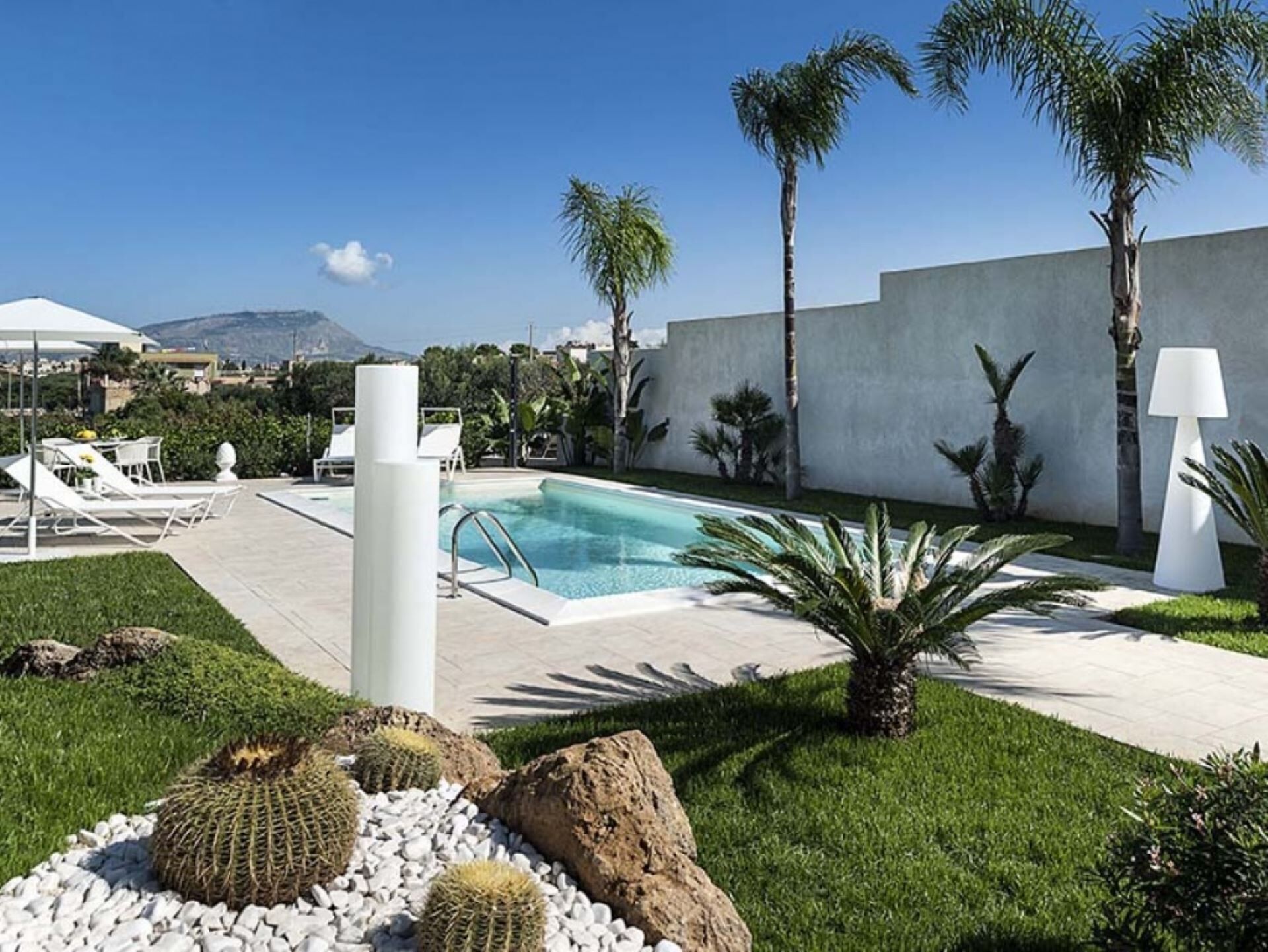 A pool area with lounge chairs, a pool, palm trees, and a modern building in the background.