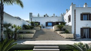 Ein modernes Gebäude mit einer zentralen Treppe, die zu einer Tür führt, umgeben von Grünflächen und blauem Himmel.