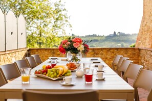 A dining table set with chairs, a fruit platter, a vase of flowers, and a view of a landscape. - Luxury refined villa with pool (Tavarnelle Val di Pesa)