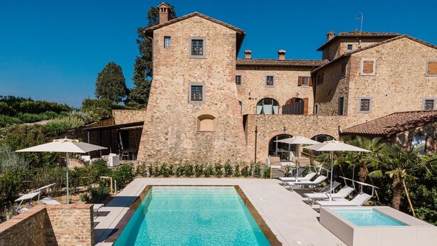 A stone building with a pool and lounge chairs.