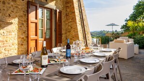 An outdoor dining area with stone walls, wooden doors, and a table set for a meal with wine glasses and plates.