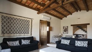 A living room with two black sofas, patterned cushions, a wooden ceiling, a patterned wall hanging, a door, and a staircase with a stone archway. - Independent villa up to 16 guests (Buseto Palizzolo)