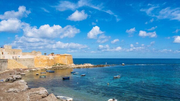 A coastal scene with a fortified building, rocky shoreline, and several small boats in the water. - Independent villa up to 16 guests (Buseto Palizzolo)