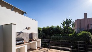 An outdoor patio with a grill, a bench, and a wall-mounted light fixture.