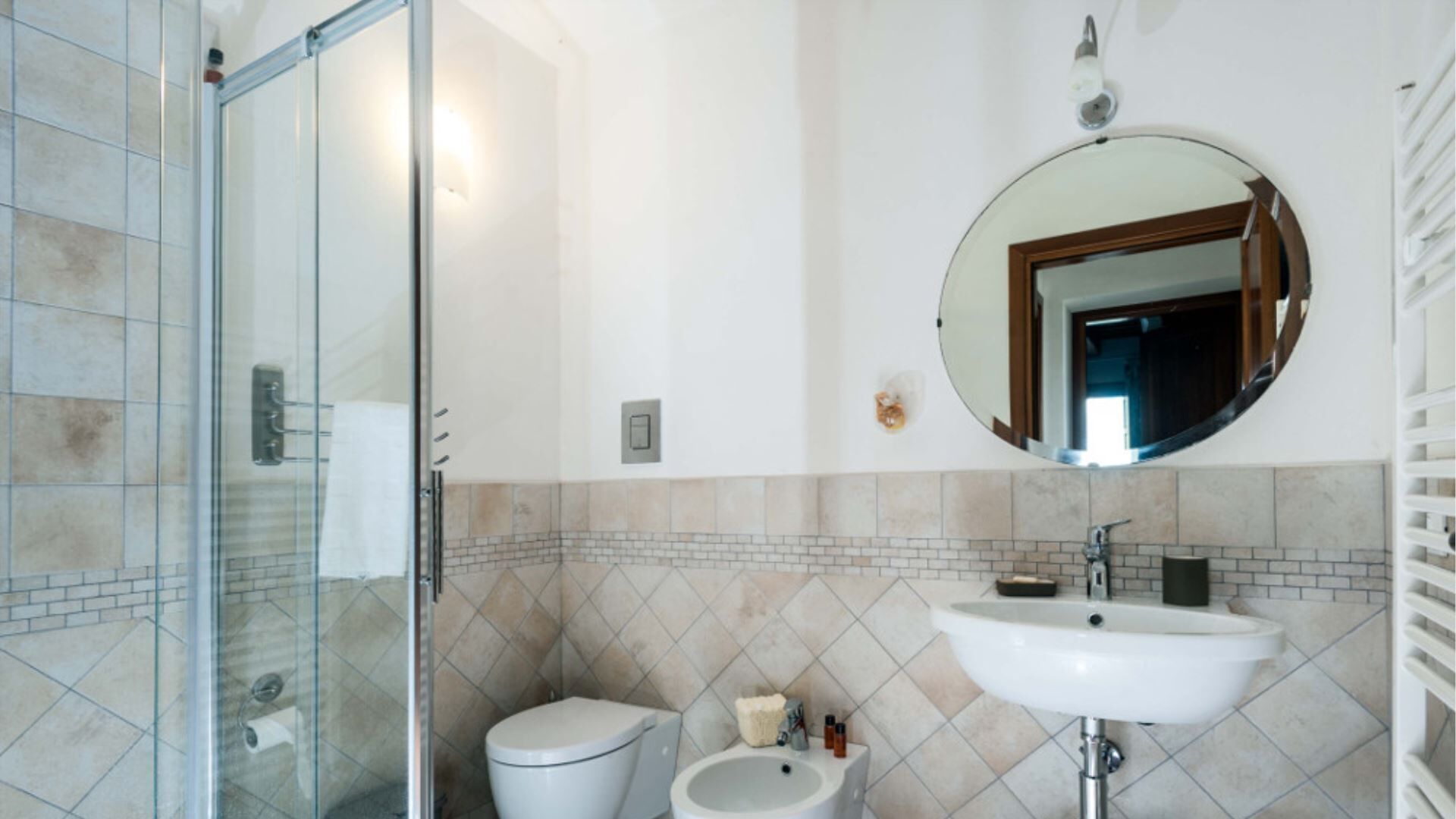 A bathroom with a glass shower enclosure, a toilet, a bidet, and a sink with a mirror above.