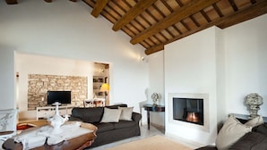 A spacious living room with a stone fireplace, a television mounted on a stone wall, and a cozy seating area with a sofa and a coffee table.