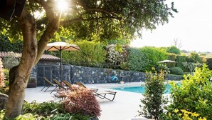 A poolside area with lounge chairs, a table with fruit and flowers, and a stone wall. - Luxurious villa on the Etna slopes, with private pool and fitness area (Viagrande)