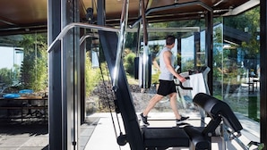 An outdoor gym with exercise equipment, a glass enclosure, and a view of greenery and a building in the background. - Luxurious villa on the Etna slopes, with private pool and fitness area (Viagrande)