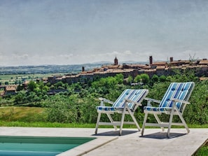 A poolside area with two striped lounge chairs, a clear view of a historic town with buildings and greenery in the background.