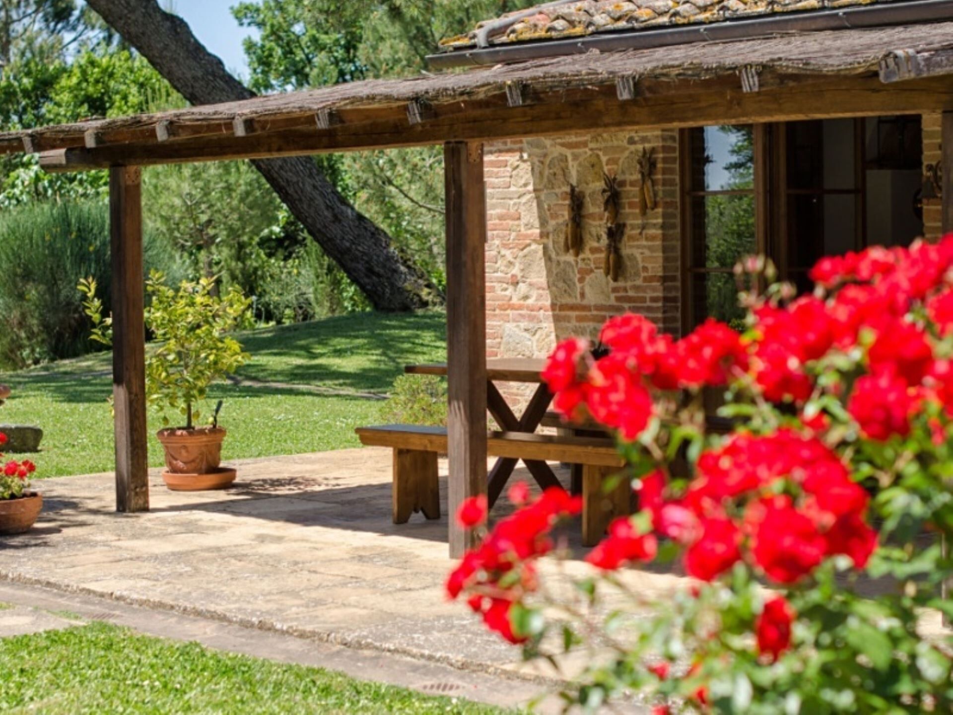 A rustic outdoor seating area with a wooden pergola, a stone wall, and a bench.