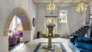 Een ruim interieur met een bakstenen boog, een ronde tafel met een bloemenvaas, een blauwe bank en een trap.