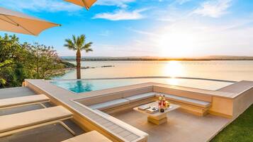 A poolside area with a view of the sunset over the water, a palm tree, and outdoor seating.