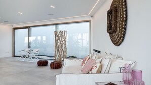 A modern living room with a large sliding glass door leading to a balcony, a white sofa with patterned cushions, and a decorative wall piece. - Dream Villa with heated pool and magnificent view on the Taormina Bay (Letoianni)