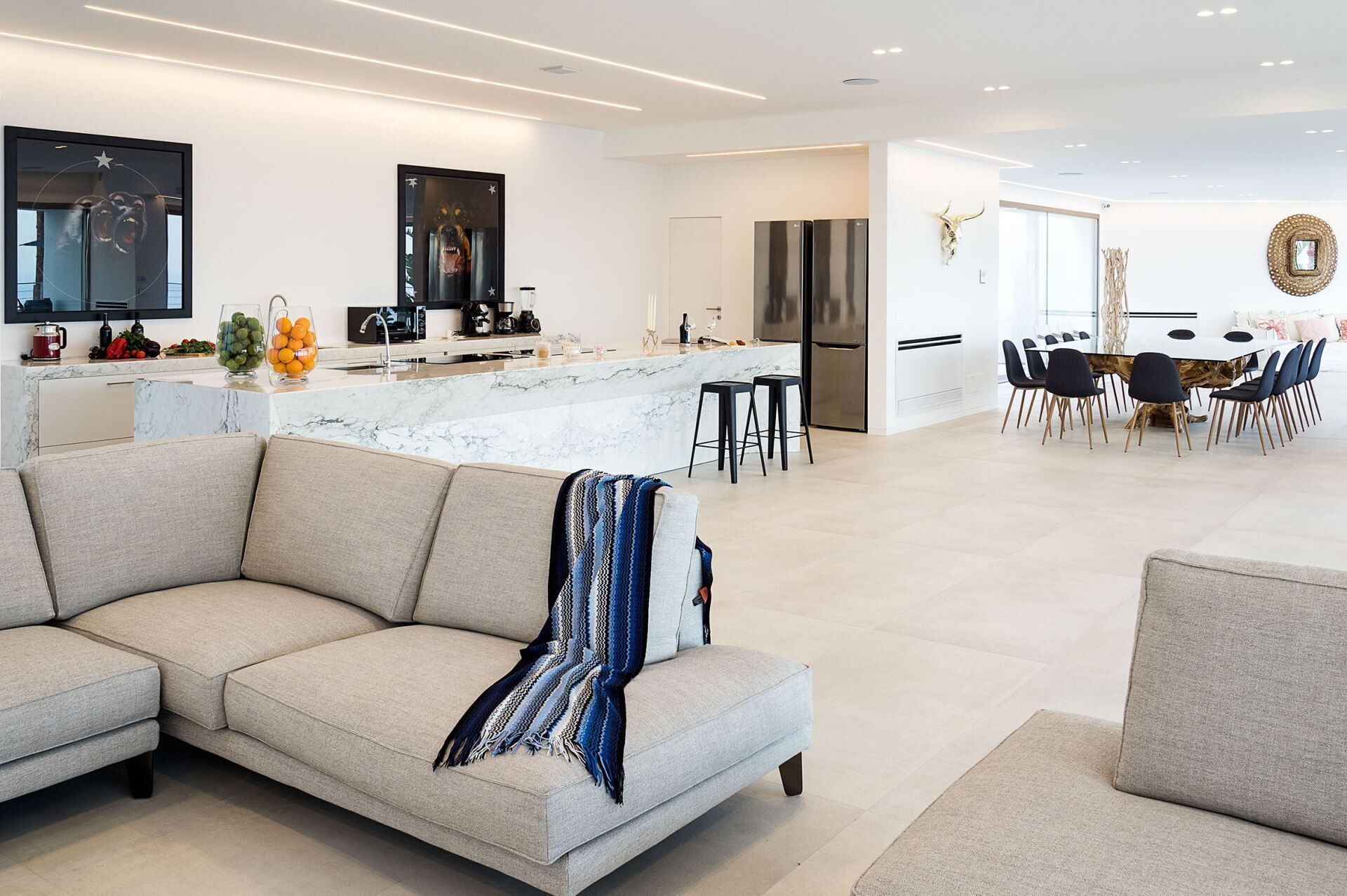 A modern kitchen with a marble countertop, a dining area with a round table and chairs, and a living area with a sofa and a throw blanket.