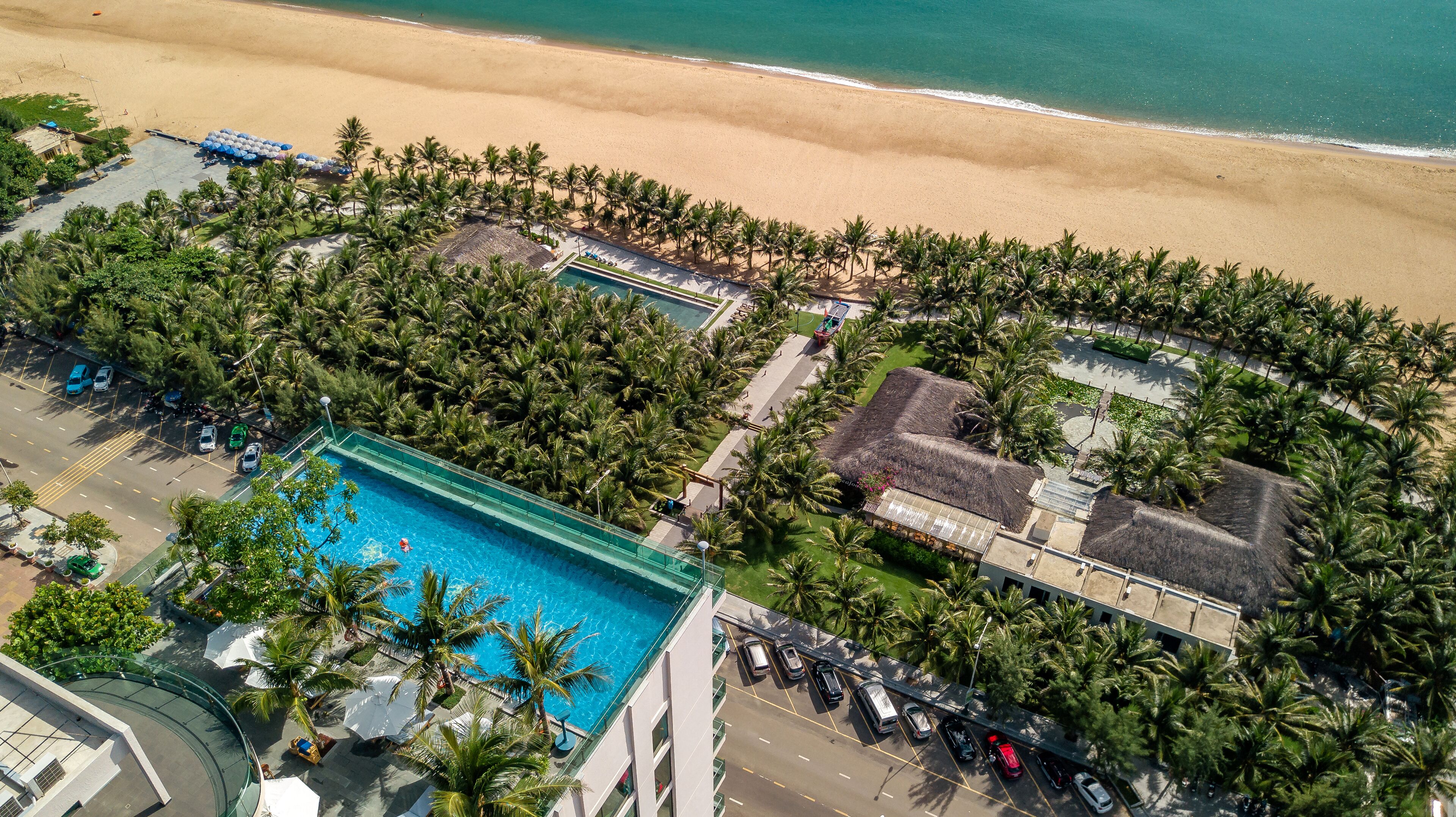 Vista aérea de un resort con piscina, playa y palmeras.