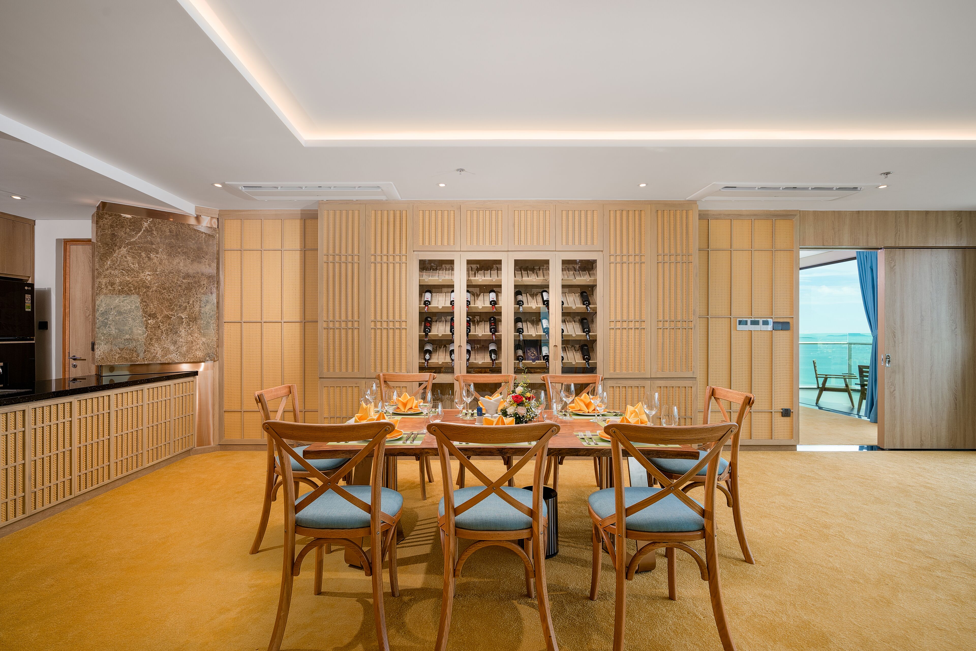 A dining area with a table set for six, wooden chairs, and a wine rack in the background.