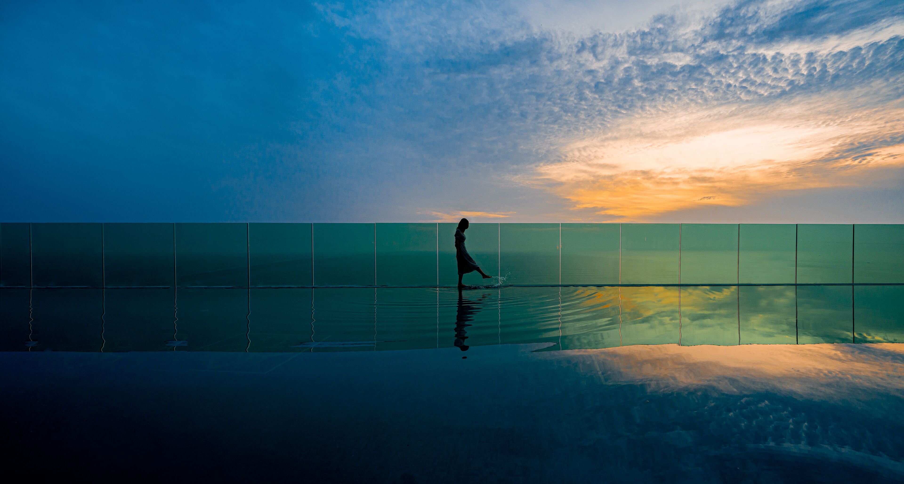 Une personne marchant sur une surface réfléchissante, avec un coucher de soleil en arrière-plan.
