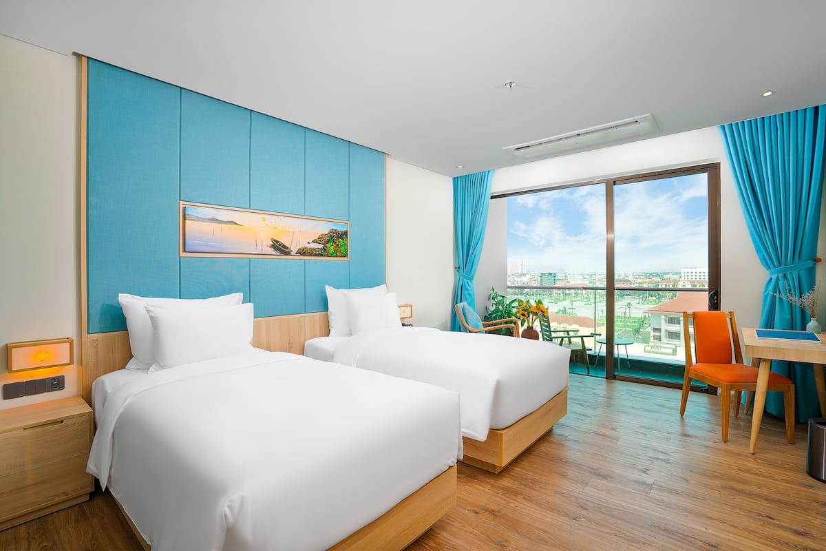 Ein Hotelzimmer mit zwei Betten, einem Schreibtisch und einem großen Fenster mit Blick auf die Stadt.