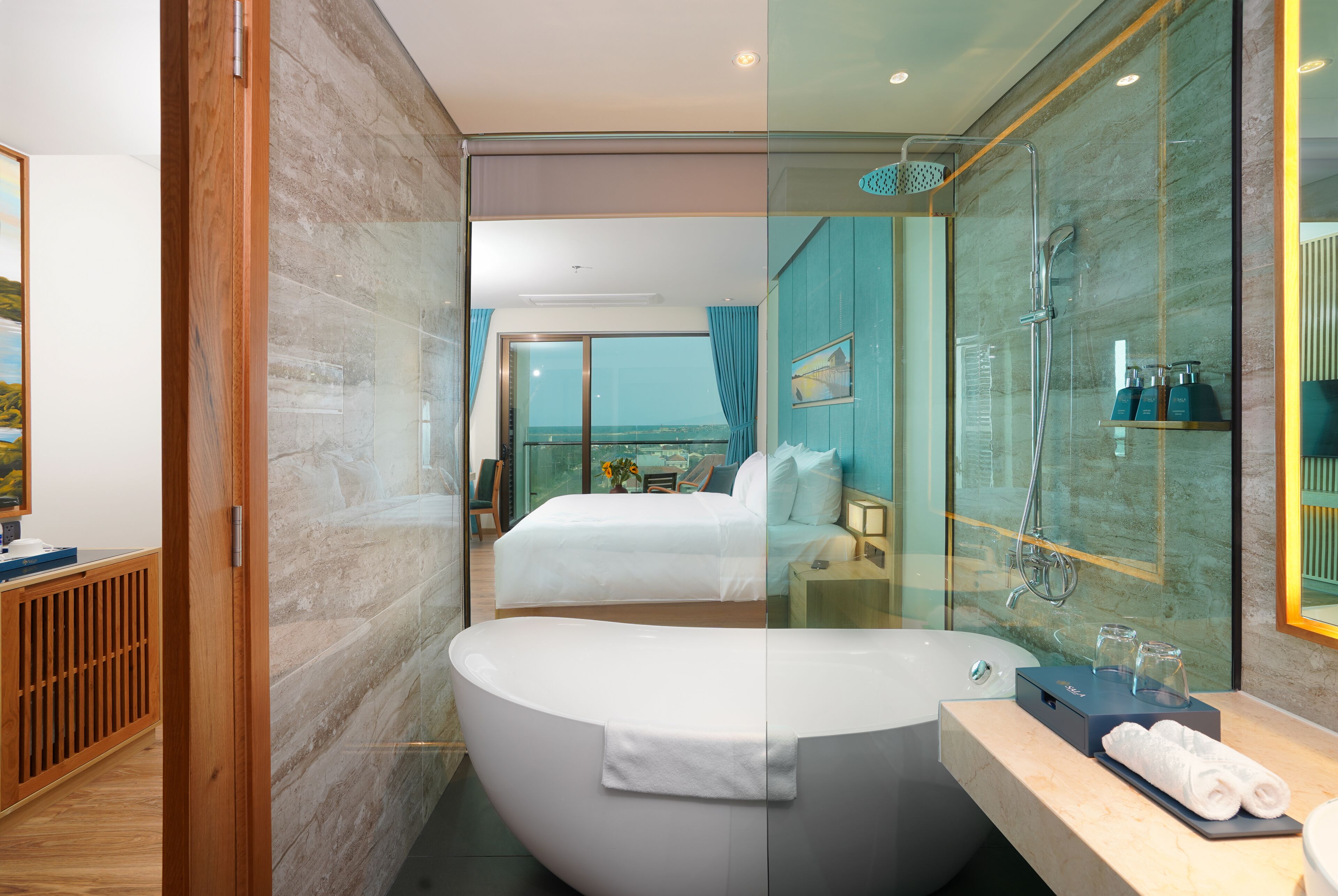 A modern hotel room with a large bathtub, a glass-enclosed shower, and a view of the sea.