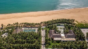 Vue aérienne d’un complexe hôtelier avec une piscine, des palmiers et une plage.
