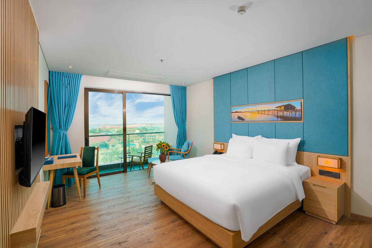 Ein Hotelzimmer mit einem großen Bett, einem Schreibtisch mit Stuhl, einem Fernseher und Blick auf die Stadt.