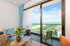 A balcony with a view of the beach, a potted plant, a chair, and a small table. - Sala Grand Tuy Hoa Hotel (Tuy Hoa)