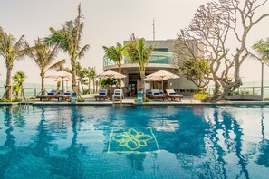 A swimming pool with lounge chairs and umbrellas, surrounded by palm trees and a modern building. - Sala Grand Tuy Hoa Hotel (Tuy Hoa)