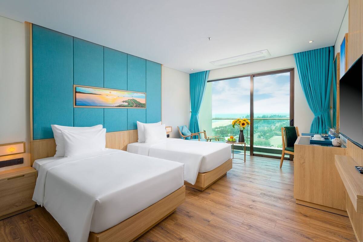 Habitación de hotel con dos camas, un escritorio, un televisor, un cuadro y vistas al exterior.