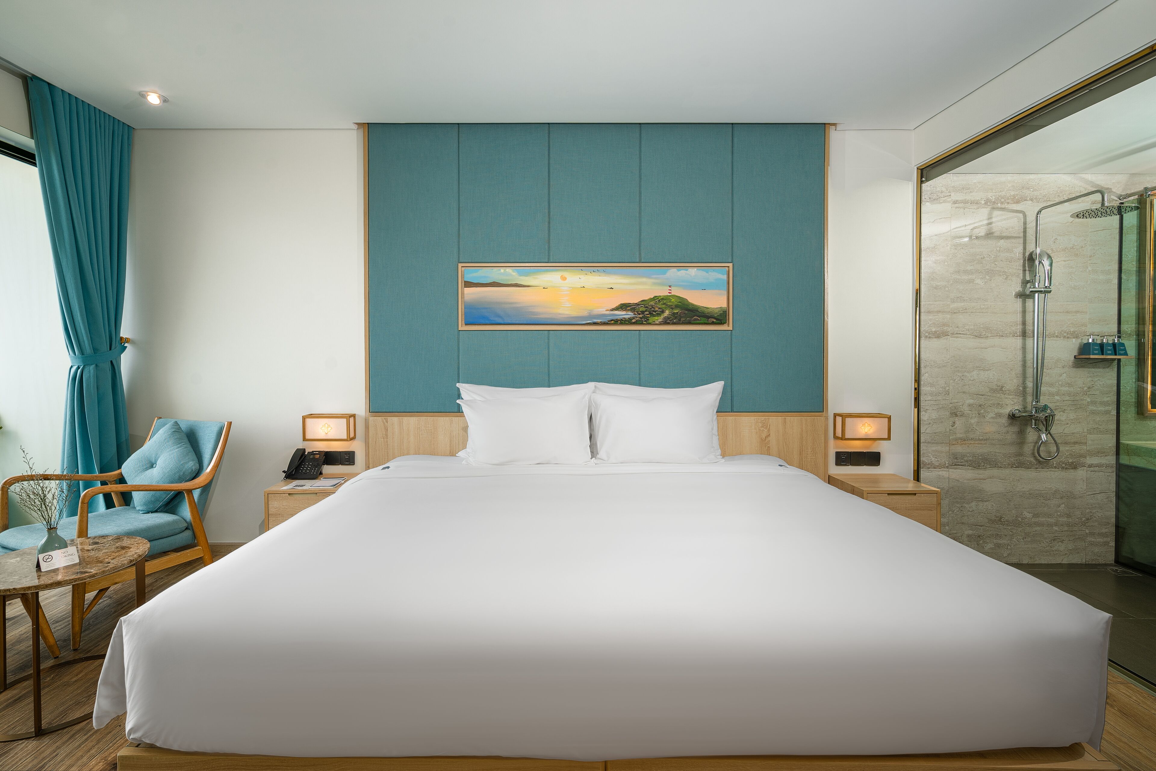 A hotel room with a large bed, a chair, a nightstand with a phone, and a painting on the wall.