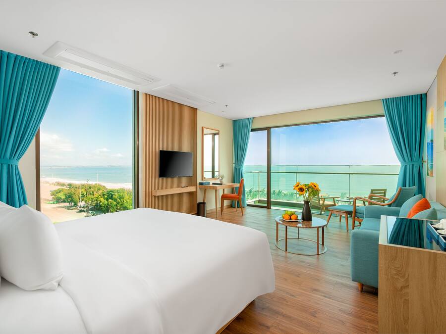 Habitació d'hotel amb un llit gran, una taula de treball, un televisor i un balcó amb vista a l'oceà.